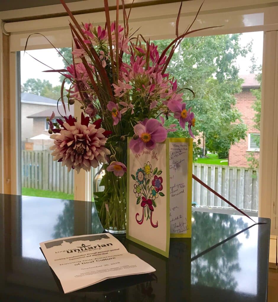 Photo of vase of flowers with a Kingston Unitarian pamphlet next to it.