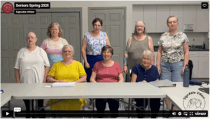 Screenshot of 8 women in 2 rows with back standing and front sitting signing the phrase
