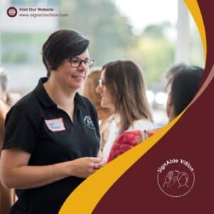 Leah Riddell, wearing a black SignAble Vi5ion shirt, is engaged in conversation with others at an event. The SignAble Vi5ion logo and website appear in the image design.